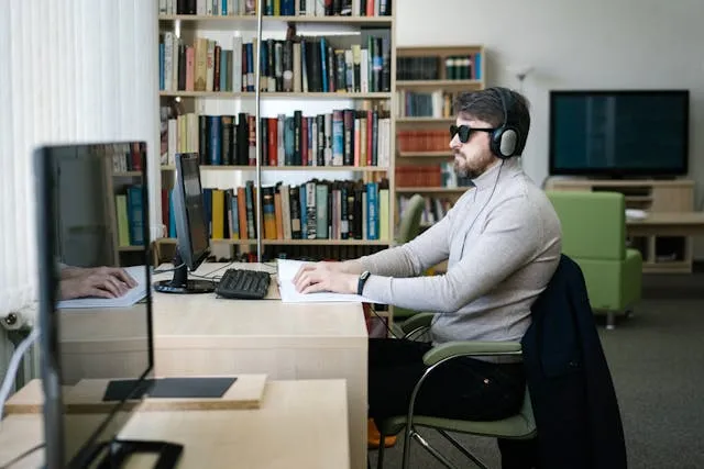 Man med synnedsättning läser en bok framför en datorskärm